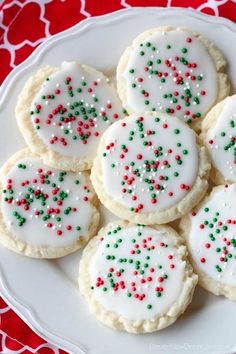 a white plate topped with cookies covered in frosting and sprinkles on top of a red table cloth