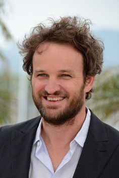 a close up of a person wearing a suit and smiling at the camera with palm trees in the background