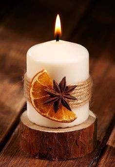 a white candle with an orange slice and star anise on it sitting on a piece of wood