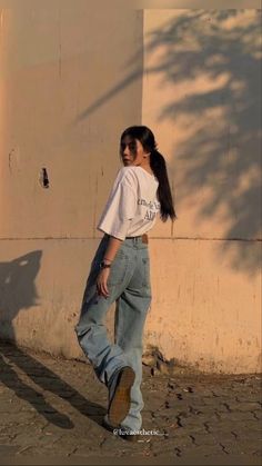 a woman standing in front of a white wall wearing jeans and a t - shirt