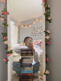 a woman taking a selfie in front of a mirror with books on the floor