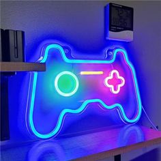 a video game controller illuminated in blue and pink neon lights on a shelf next to a clock