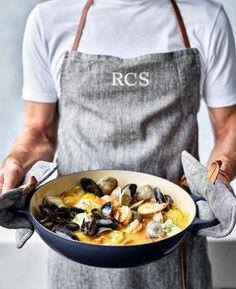 a man holding a pan full of seafood and clams in it's hands