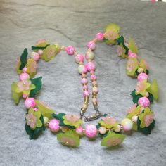 To make the flowers featured in this necklace two different shaped yellow Lucite flowers are layered with smaller pink Lucite flowers, and for every third one a Lucite leaf is added, and in the middle of each flower is a pale-yellow Czech Crystal rondelle bead. Eleven triplets of these flowers make up most of the front of the necklace, between the flower triplets are two 6mm pink and yellow patterned Glass beads having between them a matching 10mm Glass beads. At the ends of the necklace are 10mm patterned beads alternating with 4mm beads. All these flowers and beads are separated by silver lined pale gold coloured Glass seed beads. All the metal work is Stainless Steel including the magnetic clasp and the earwires on the free matching earrings. Necklace and earring come enclosed within a Red Jewellery, Graduation Necklace, Red Jewelry, Yellow And Pink, Silver Line, Pattern Glass, Yellow Pattern, Czech Crystal, Beading Wire