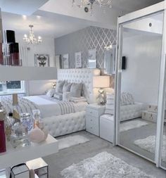 a bedroom with white furniture and chandelier hanging from the ceiling in front of a large mirror