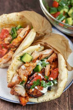 two chicken pita sandwiches on a plate with tomatoes and cucumbers in the background