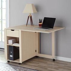 a laptop computer sitting on top of a wooden desk next to a lamp and window