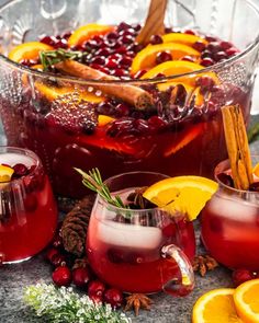 two glasses filled with cranberry punch surrounded by orange slices, cinnamon and spices