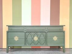 a green dresser with gold handles in front of a multicolored wall and floor