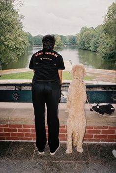 a woman standing next to a white dog on top of a brick wall near a river