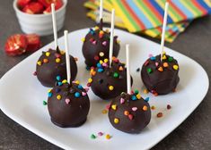 chocolate covered cake pops with sprinkles on a white plate next to a bowl of strawberries