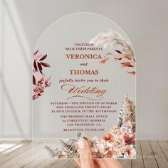 a person holding up a wedding card with flowers on it