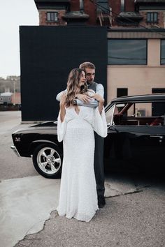 a man and woman standing in front of a black car with their arms around each other