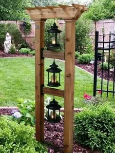 a wooden stand with lanterns on it in front of some bushes and trees, next to a lawn