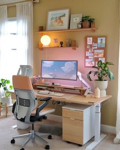 a desk with a computer on top of it in front of a potted plant