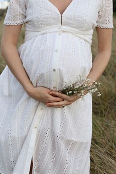 a pregnant woman in a white dress holding a flower