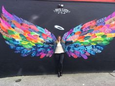 a woman standing in front of a wall with colorful wings painted on it's side