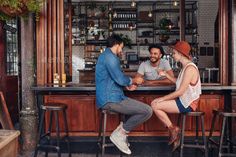 two men and a woman sitting at the bar