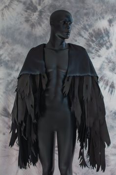 a male mannequin with black feathers on it's chest and arms, standing in front of a tie dyed background