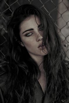 a woman with long hair standing next to a fence