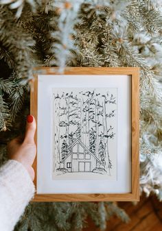 a person holding up a framed drawing in front of a christmas tree with pine needles