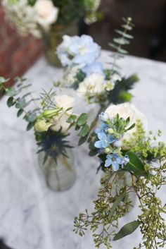 three vases filled with flowers sitting on top of a white marble tablecloth covered table