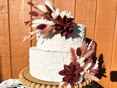 a three tiered cake with red and white flowers on the top is sitting on a wooden stand