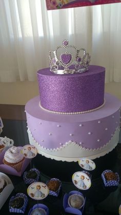 there is a purple cake with a crown on top and cupcakes around it