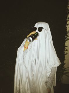 a person dressed in a ghost costume holding a bottle and cell phone to their ear