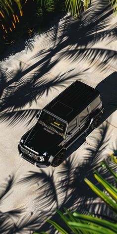 an aerial view of a black car parked in the sand with palm trees behind it