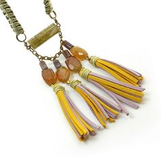 Tribal tassel fringe necklace with gemstones.This necklace is absolutely unique and its neutral colors make it a versatile accessory to any outfit. The focal unit of this necklace is made up of a large moss green cylindrical agate gemstone , jasper mini cylindrical stone beads and amber colored agate gemstones. From the gemstone dangle funky faux leather tassels in mustard yellow and pale pink. The elegant and detailed straps of this necklace are made up of dull gold cord that is intricately wov Fringe Jewelry, Tassel Necklace Boho, Textile Necklace, Long Tassel Necklace, Stone Statement Necklace, Long Statement Necklace, Yellow Necklace, Boho Chic Jewelry, Spring Jewelry