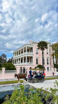 a horse drawn carriage in front of a large pink building with white pillars and balconies