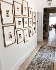 a hallway with many framed pictures on the wall and a rug in front of it