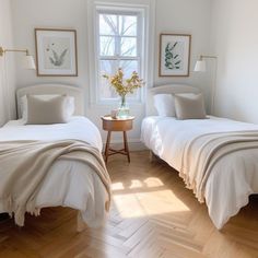 two beds in a room with white walls and wood flooring, one has a vase on the end table