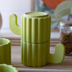 a green cactus shaped teapot sitting on top of a bamboo mat next to two mugs