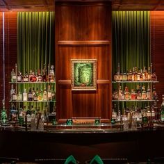 the bar has many bottles on it and green curtains in the back ground, behind which is a painting with a man's face