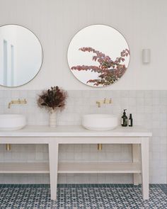 there are two sinks in the bathroom with mirrors on the wall above them and a vase filled with flowers