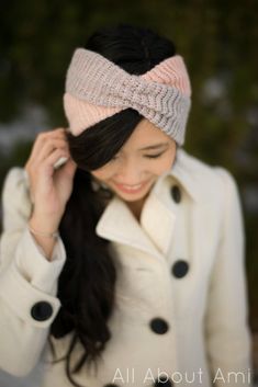 a woman wearing a white coat and a pink knitted headband is talking on her cell phone