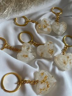 five key chains with white flowers and gold accents on them sitting on a white cloth