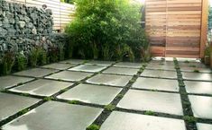 an outdoor patio with stone tiles and grass growing on the ground, next to a wooden fence