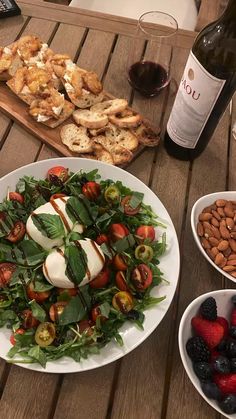 a plate of salad with dressing, fruit and bread on a table next to wine