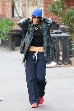 a woman walking down the street with her hand on her head and wearing a blue hat