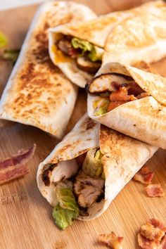 three burritos with meat, lettuce and bacon on a cutting board