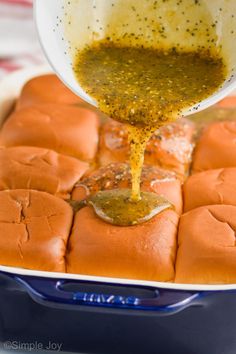 someone pouring mustard on top of hot dogs in a baking pan with other food items