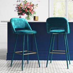 two green velvet bar stools in front of a blue counter with flowers on it