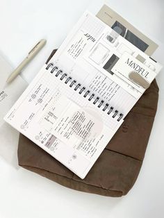 an open planner and pen sitting on top of a brown piece of paper next to a notepad