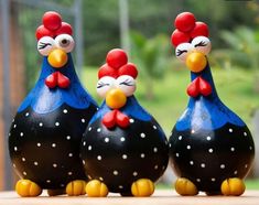 three ceramic chickens sitting next to each other on top of a wooden table with grass in the background