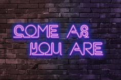 a neon sign that says, come as you are on the side of a brick wall