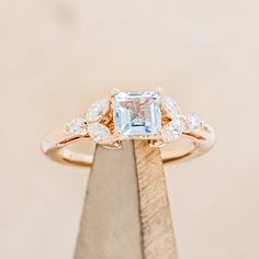 an engagement ring with a blue topazte surrounded by white diamonds on a wooden stand