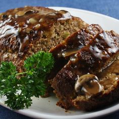 meatloaf with mushrooms and gravy on a white plate, garnished with parsley